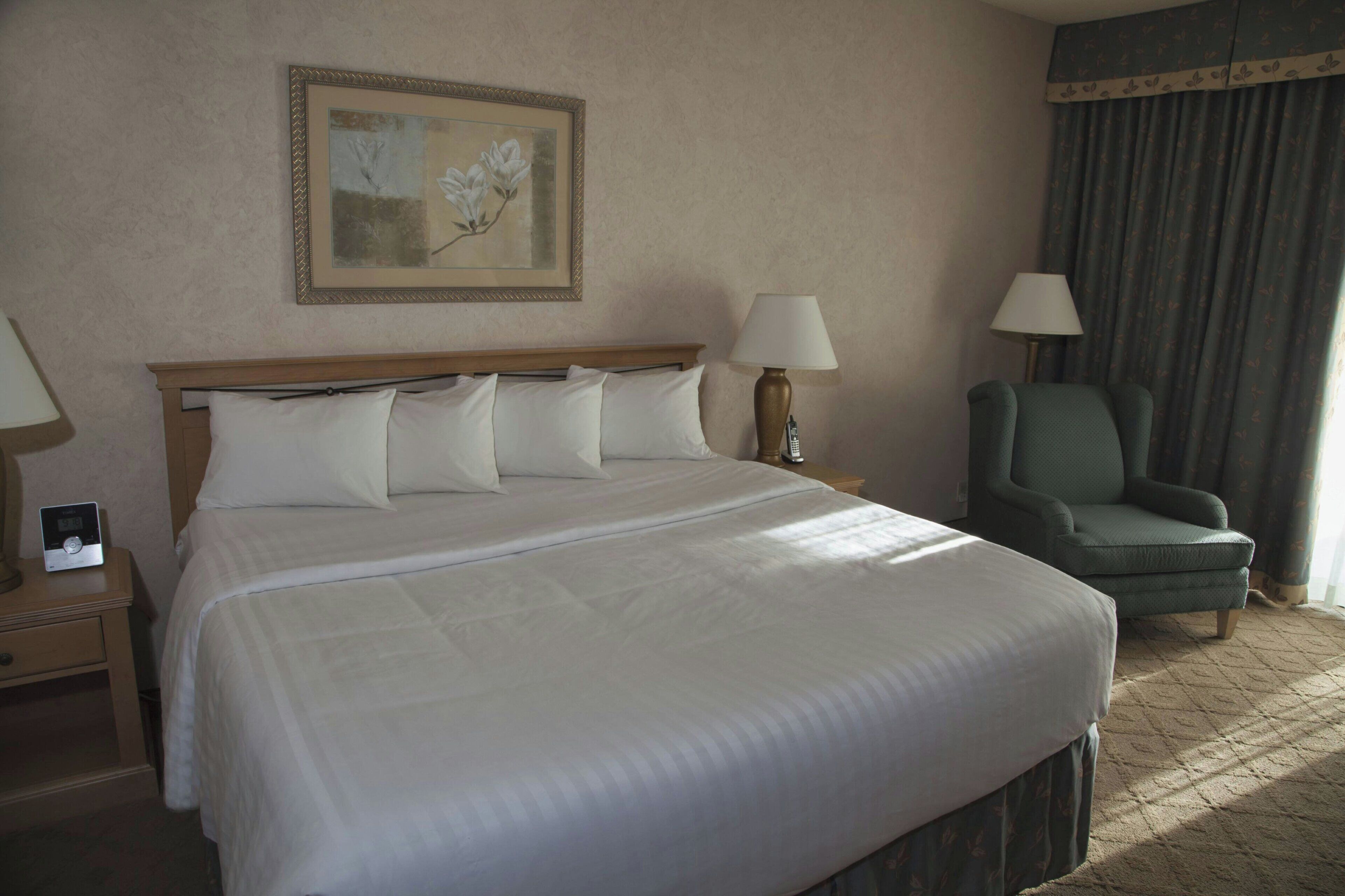 Una habitación de hotel con una cama grande, dos lámparas de noche, una silla y un cuadro en la pared.