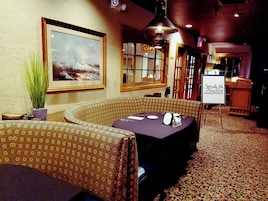Interior de un restaurante con una mesa para dos, un cuadro grande en la pared y un cartel que dice 'Steak & Anchor'.