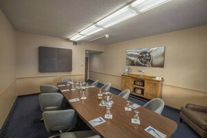 A conference room with a long table, chairs, a coffee station, and a painting on the wall.