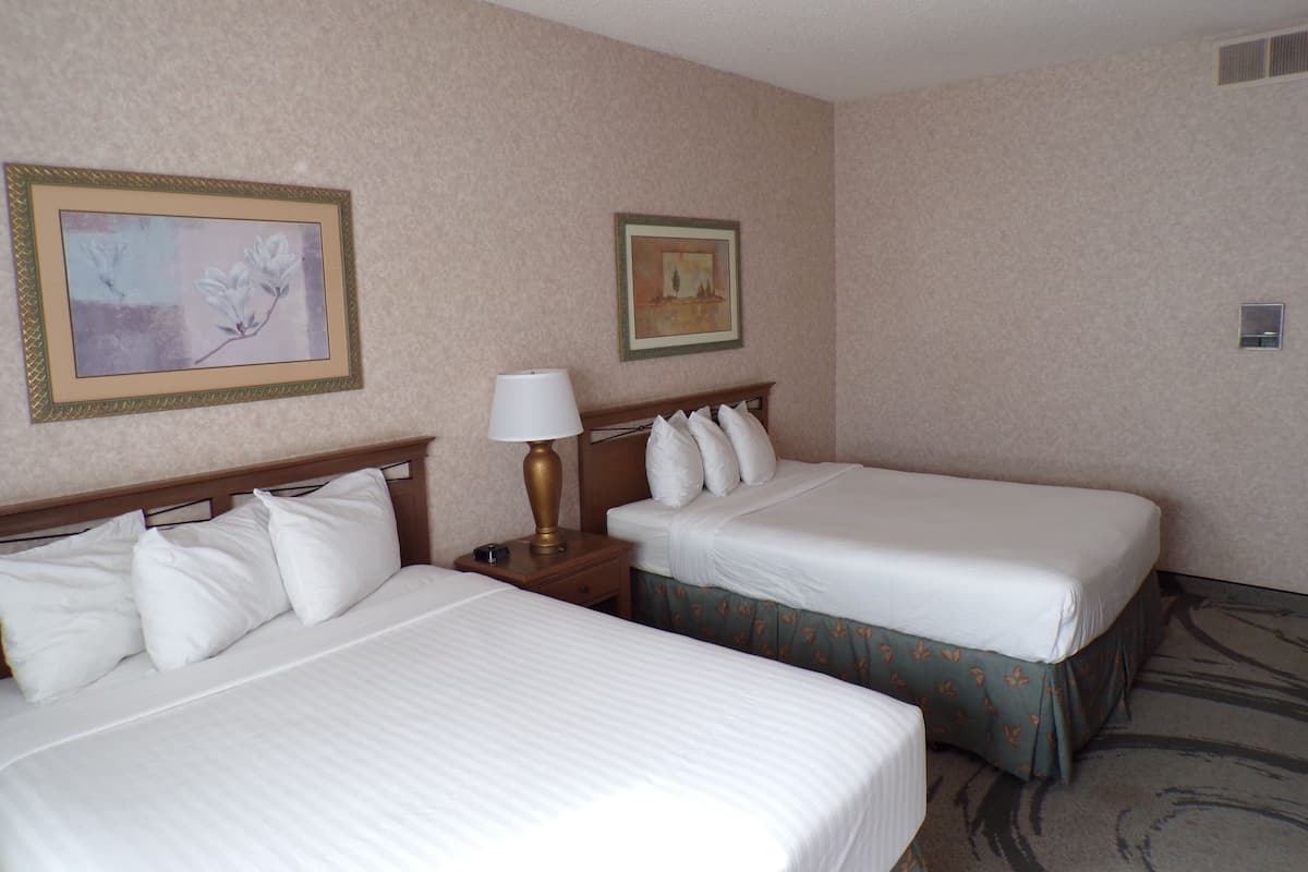 Une chambre d’hôtel avec deux lits, une table de chevet avec une lampe et deux tableaux encadrés au mur.