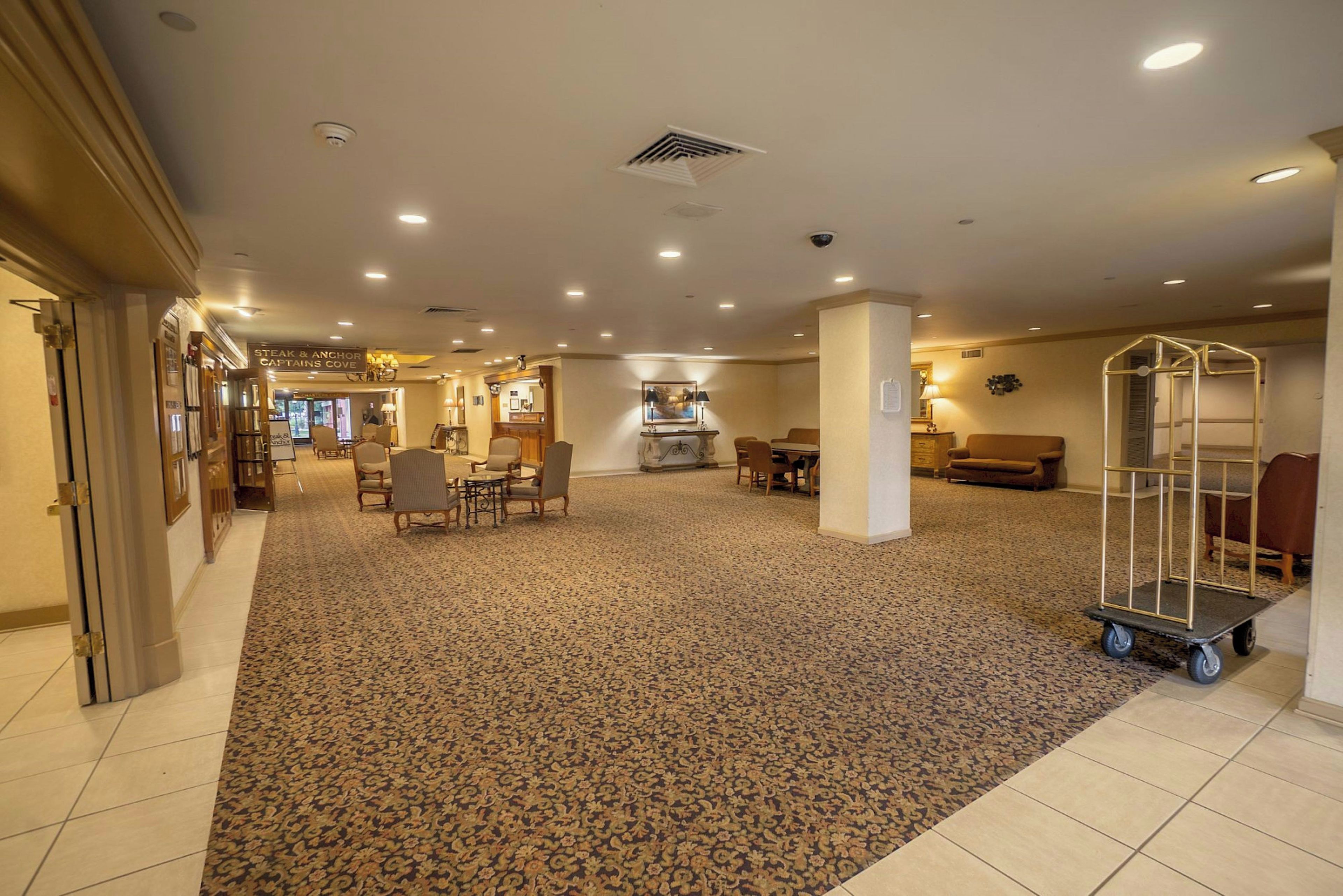 A hotel lobby with a carpeted floor, seating area, and a dining section.
