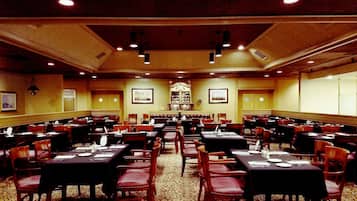 A large banquet hall with multiple tables and chairs, a high ceiling with recessed lighting, and framed pictures on the walls.