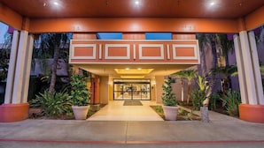 A hotel entrance with a covered walkway, palm trees, and a glass door leading inside.