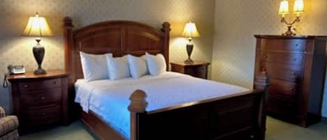 Quarto com cama de madeira, duas mesas de cabeceira com abajures, um criado-mudo e cômoda, além de parede estampada.