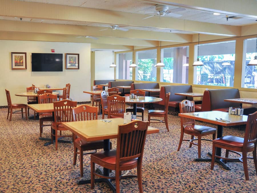 A restaurant with multiple tables and booths, carpeted flooring, and large windows.