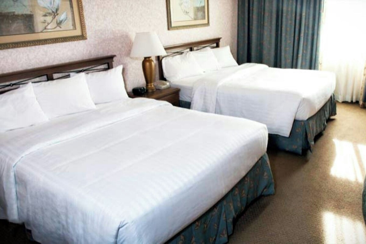 Une chambre d’hôtel avec deux lits, une table de chevet, une lampe, une chaise et une fenêtre avec des rideaux.