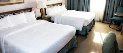 Habitación de hotel con dos camas, una mesita de noche, una lámpara, una silla y una ventana con cortinas.