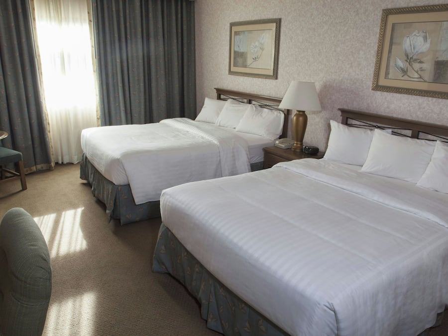 A hotel room with two beds, a desk, a chair, and a window with curtains.