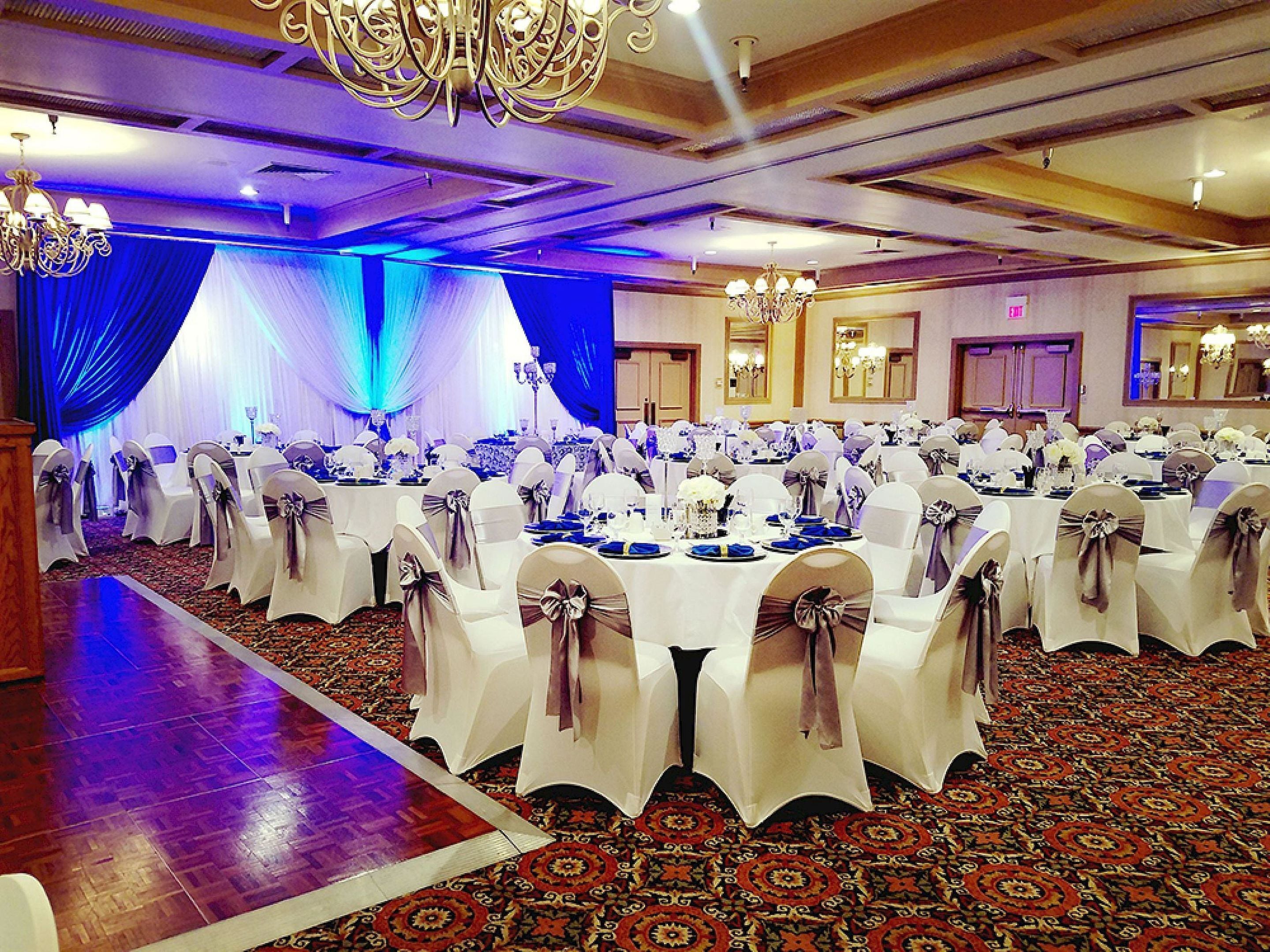 A banquet hall with round tables, white tablecloths, and chairs with bows.