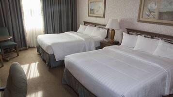 A hotel room with two beds, a chair, a table, and a lamp.