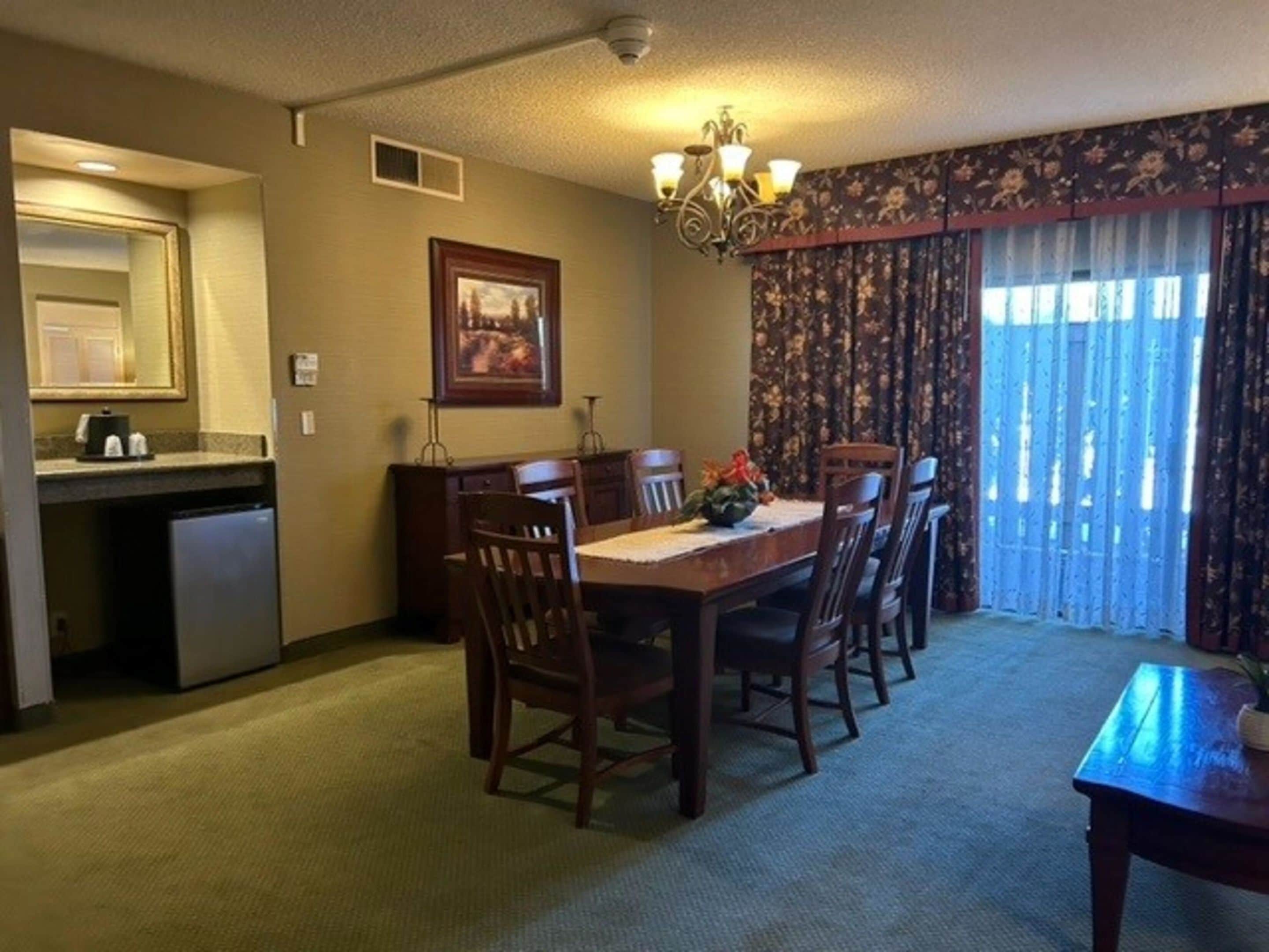 A dining area with a table, chairs, a chandelier, a painting, and a window with curtains.