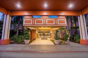 L’entrée d’un hôtel, avec un passage couvert, des plantes en pot et une porte d’entrée en verre.