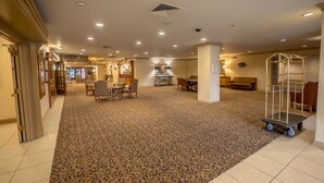 A hotel lobby with a carpeted floor, seating areas, a reception desk, and a food service area.
