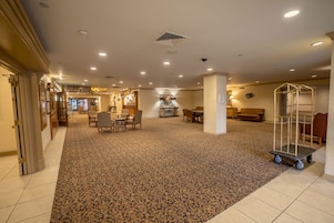 A hotel lobby with a carpeted floor, seating areas, a reception desk, and a food service area.