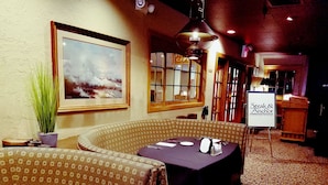 A restaurant with a table set for two, a large painting on the wall, and a sign for 'Steak & Anchor.'