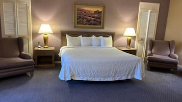 Une chambre d’hôtel avec un grand lit, deux fauteuils, une table de chevet avec une lampe et un tableau au mur.