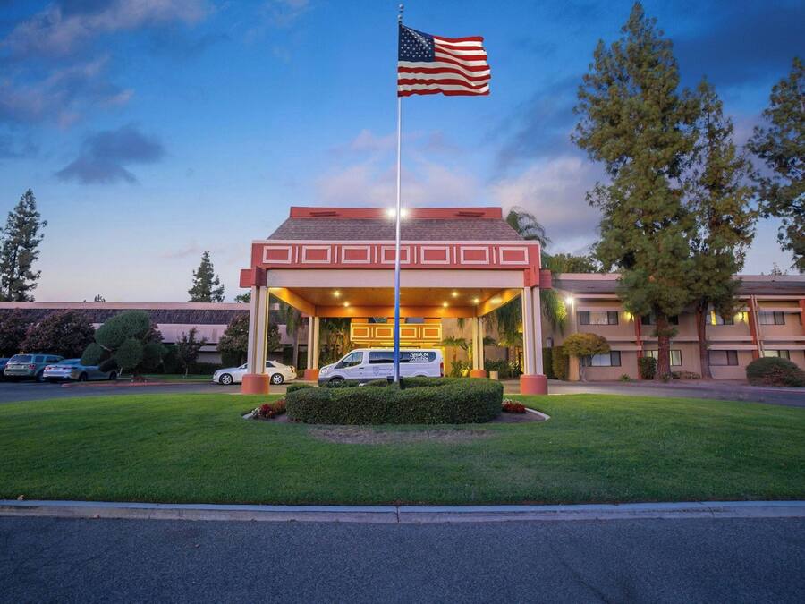 A hotel entrance with a flag, a covered parking area, and a building with a flat roof.