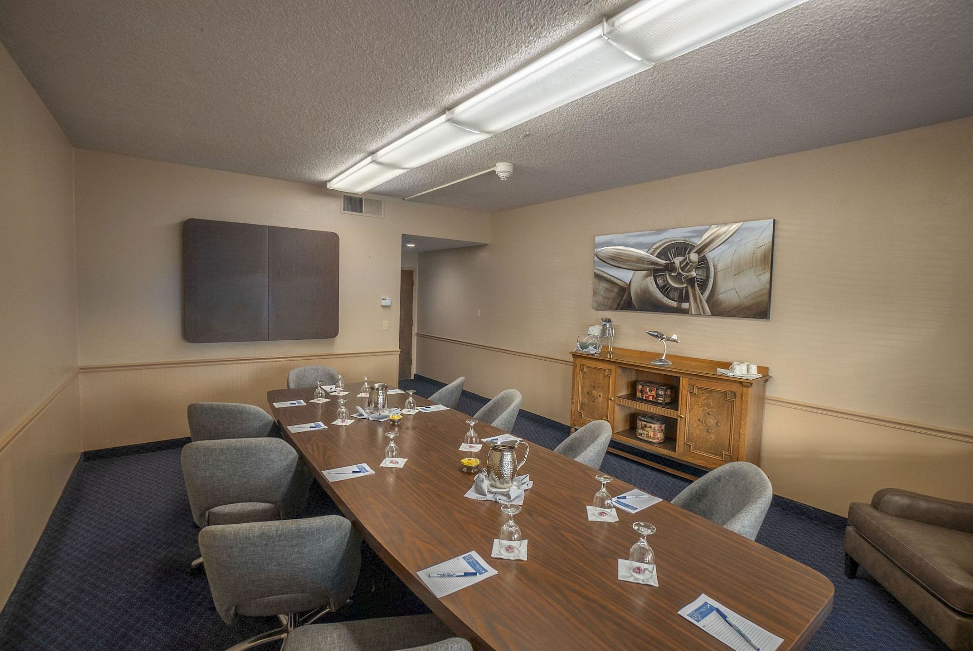 A conference room with a long table, chairs, a wooden cabinet, and a painting on the wall.