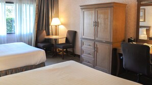 Una habitación de hotel con dos camas, un escritorio con lámpara, un armario y un espejo.