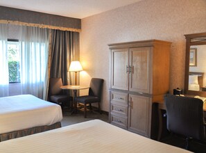 Une chambre d’hôtel avec deux lits, un bureau avec une lampe, une armoire et un miroir.