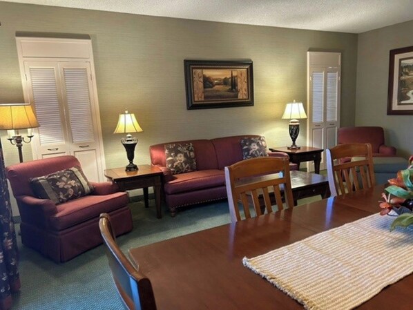 A living room with a sofa, chairs, a dining table, lamps, and a framed picture on the wall.