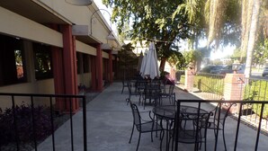Un patio al aire libre con mesas y sillas, un camino y un edificio con columnas y ventanas.