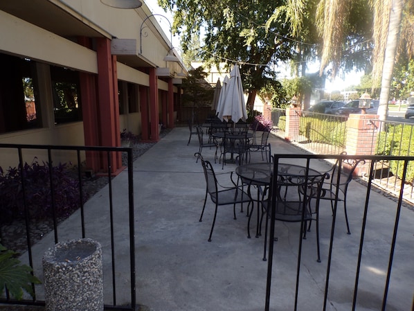 An outdoor patio with tables and chairs, a pathway, and a building with columns and windows. - Piccadilly Inn Airport (Fresno)