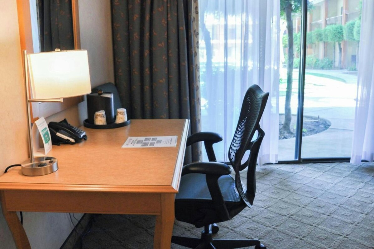 Une chambre d’hôtel équipée d’un bureau, d’une chaise, d’une lampe, d’un téléphone et d’une fenêtre avec des rideaux.