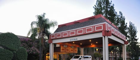 A hotel entrance with a covered waiting area, a van parked in front, and a clear sign indicating a 11ft clearance.