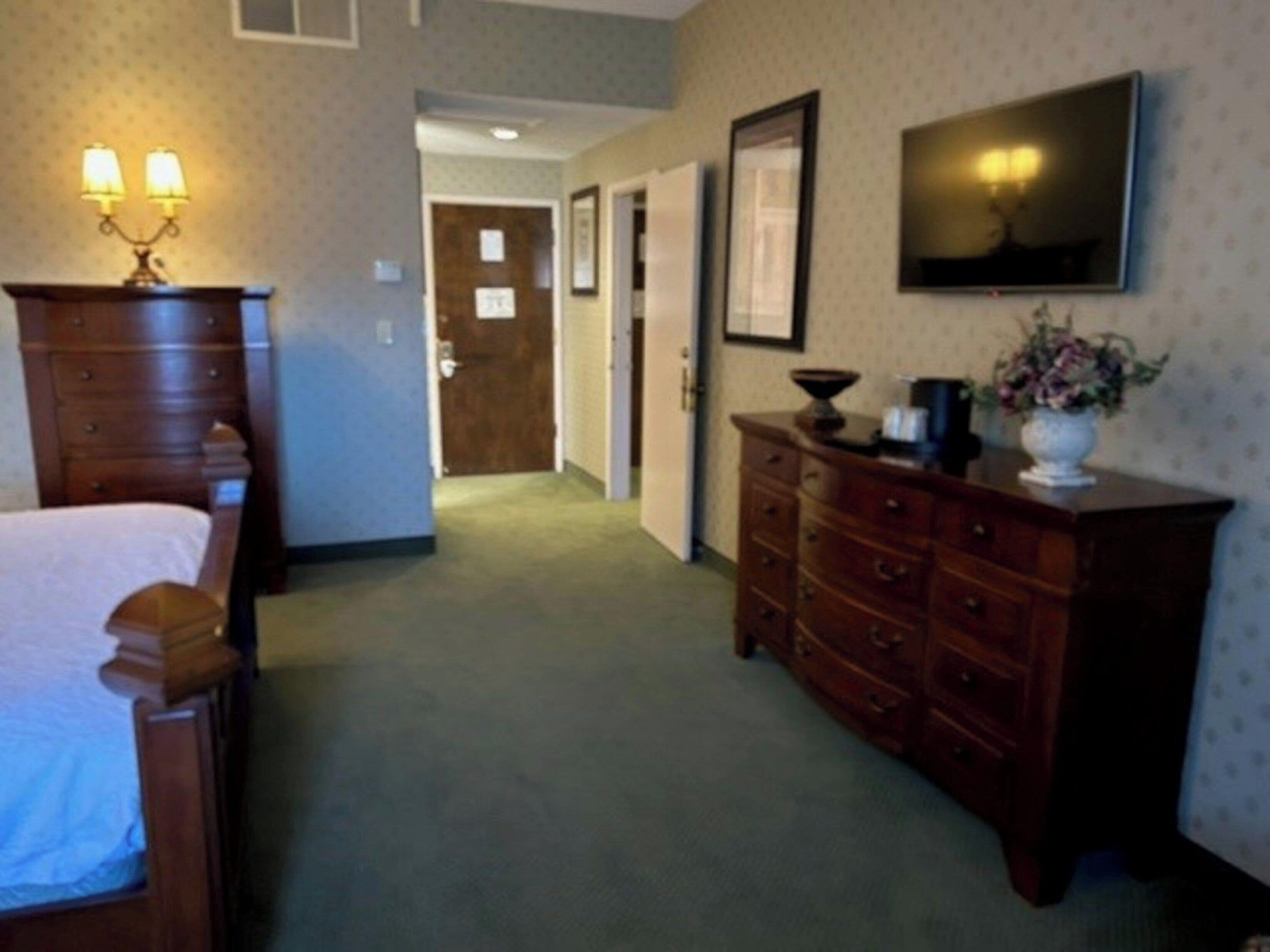 Un couloir d’hôtel avec une commode en bois, un lit et un téléviseur fixé au mur.