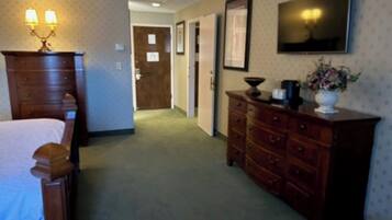 Un couloir d’hôtel avec une commode en bois, un lit et un téléviseur fixé au mur.