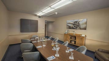 Sala de conferência com uma mesa comprida, cadeiras, cantinho de café e um quadro na parede.