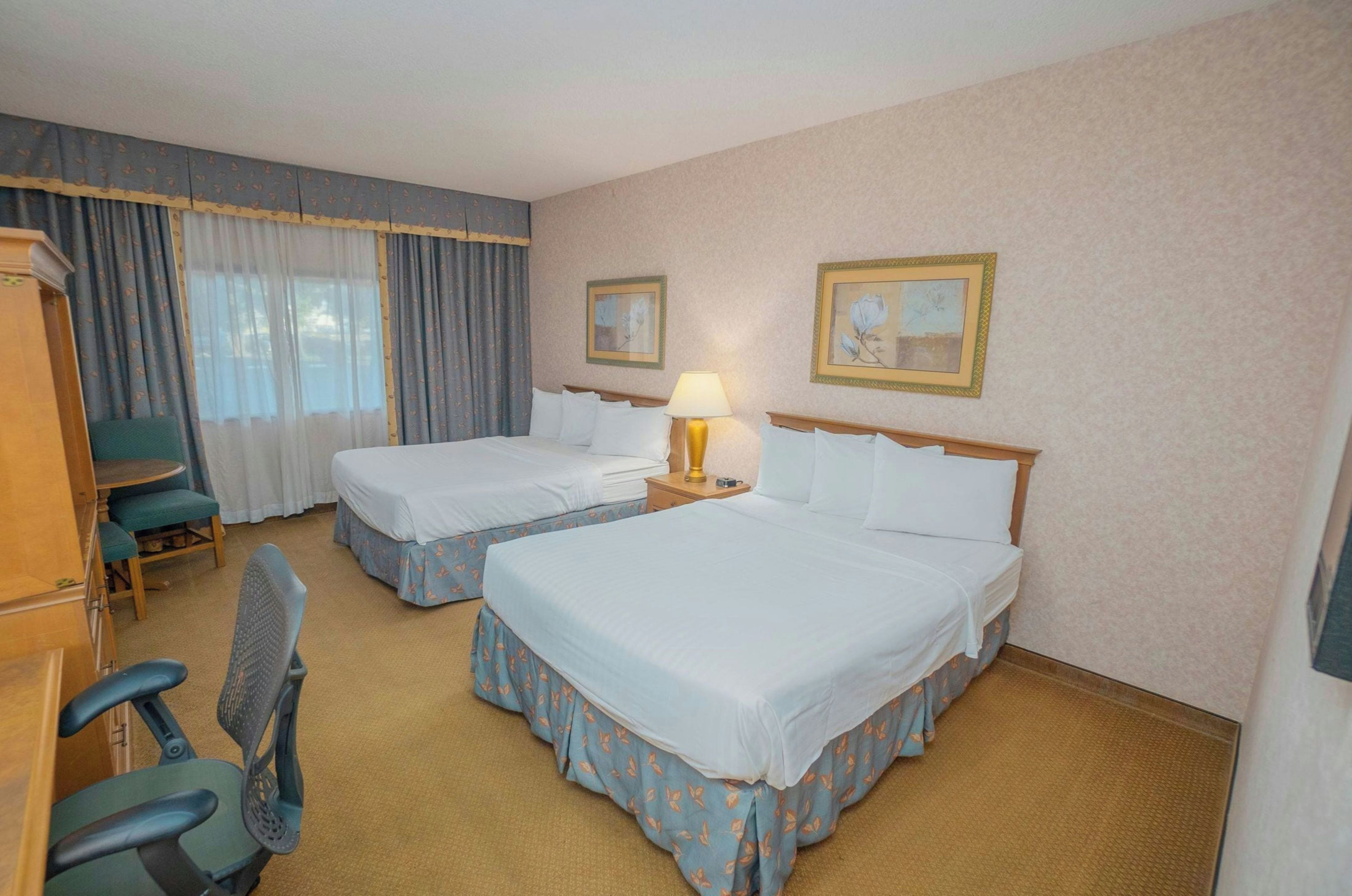 Habitación de hotel con dos camas, un escritorio, una silla y una lámpara.