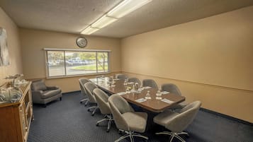 A conference room with a large table, six chairs, a clock on the wall, and a window with blinds.