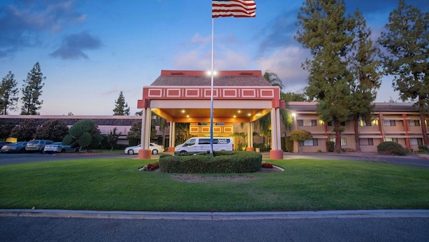 A hotel entrance with a flag, a covered parking area, and a building with a flat roof.