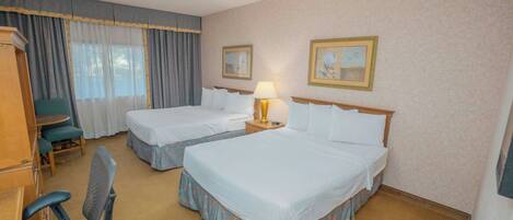 A hotel room with two beds, a desk, a chair, and a lamp.