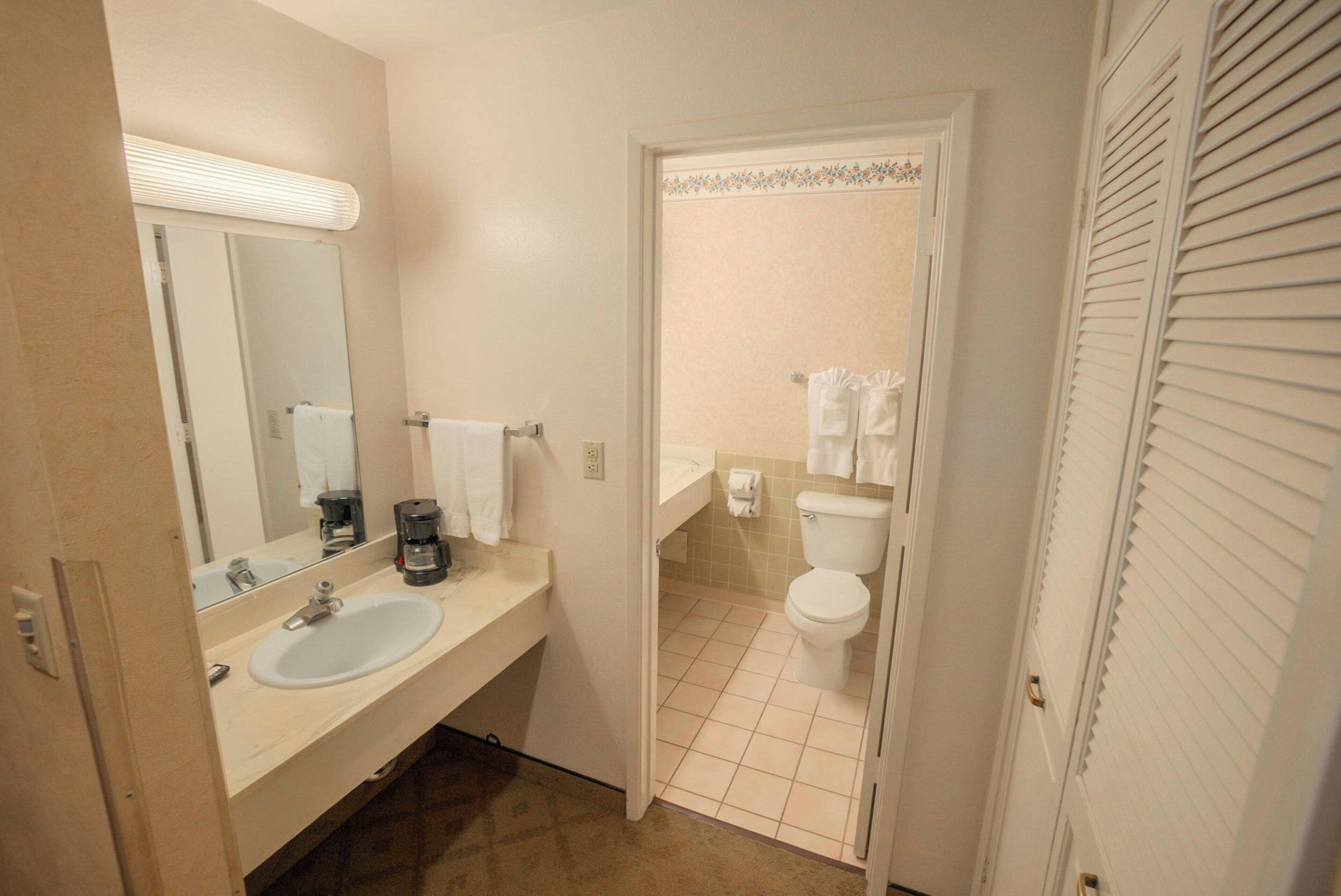 Une salle de bain d’hôtel équipée d’un lavabo, d’un miroir, de toilettes et d’un porte-serviettes.