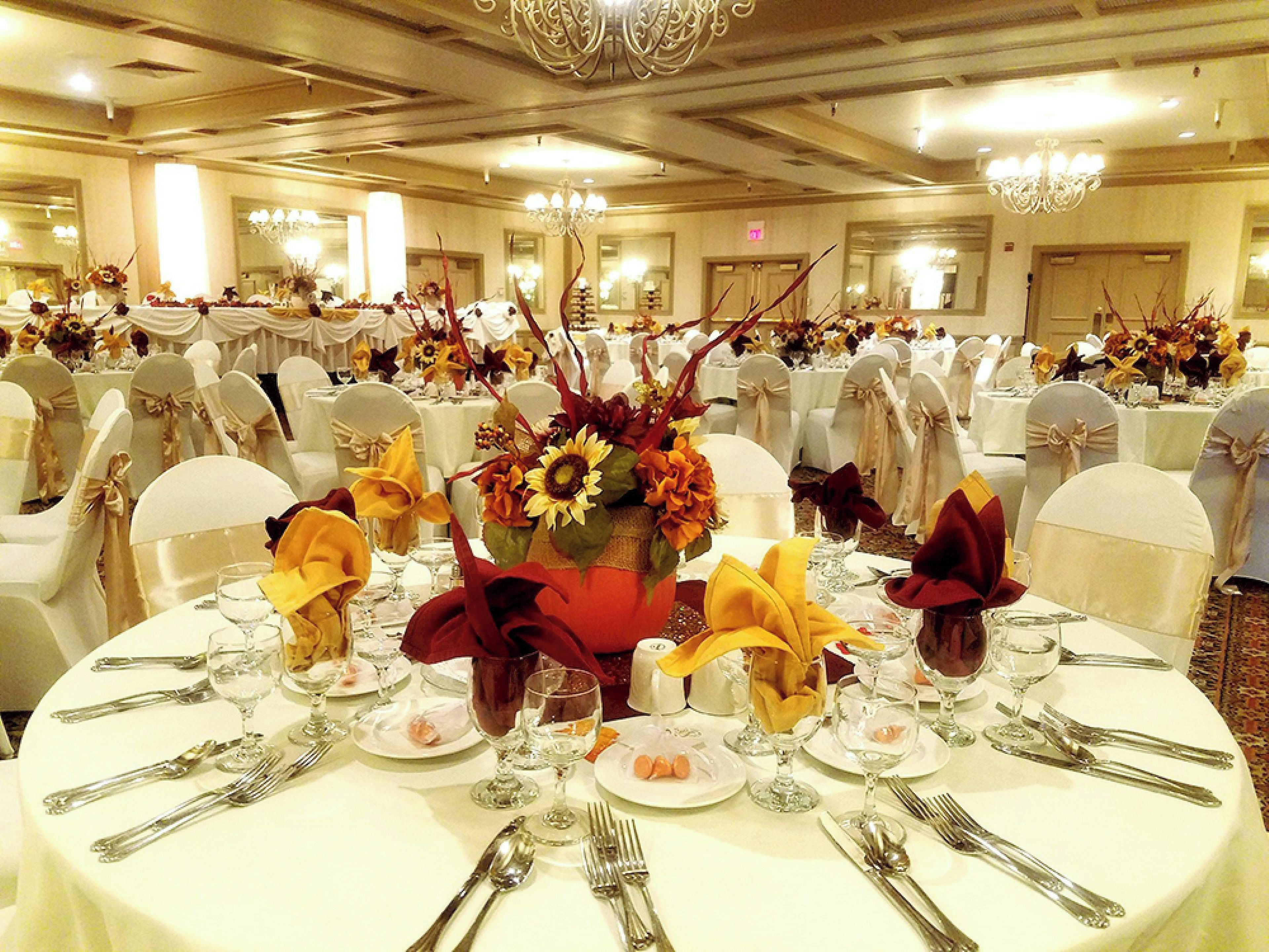 Une salle de banquet avec des tables rondes dressées pour un événement formel, agrémentée de compositions florales et de nappes blanches.