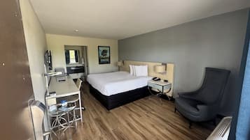 Quarto de hotel com cama, mesa de cabeceira, cadeira, escrivaninha e pequena mesa com cadeira.
