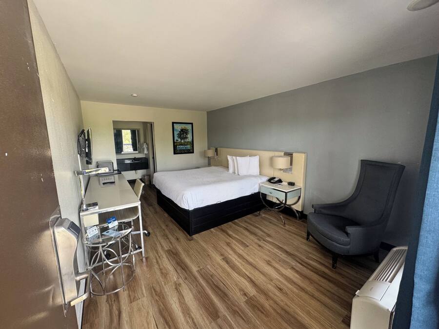 Quarto de hotel com cama, mesa de cabeceira, cadeira, escrivaninha e pequena mesa com cadeira.