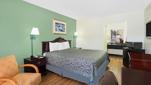 Habitación de hotel con cama, dos lámparas de noche, mesita de noche, una silla, escritorio, televisor y zona de cocina.