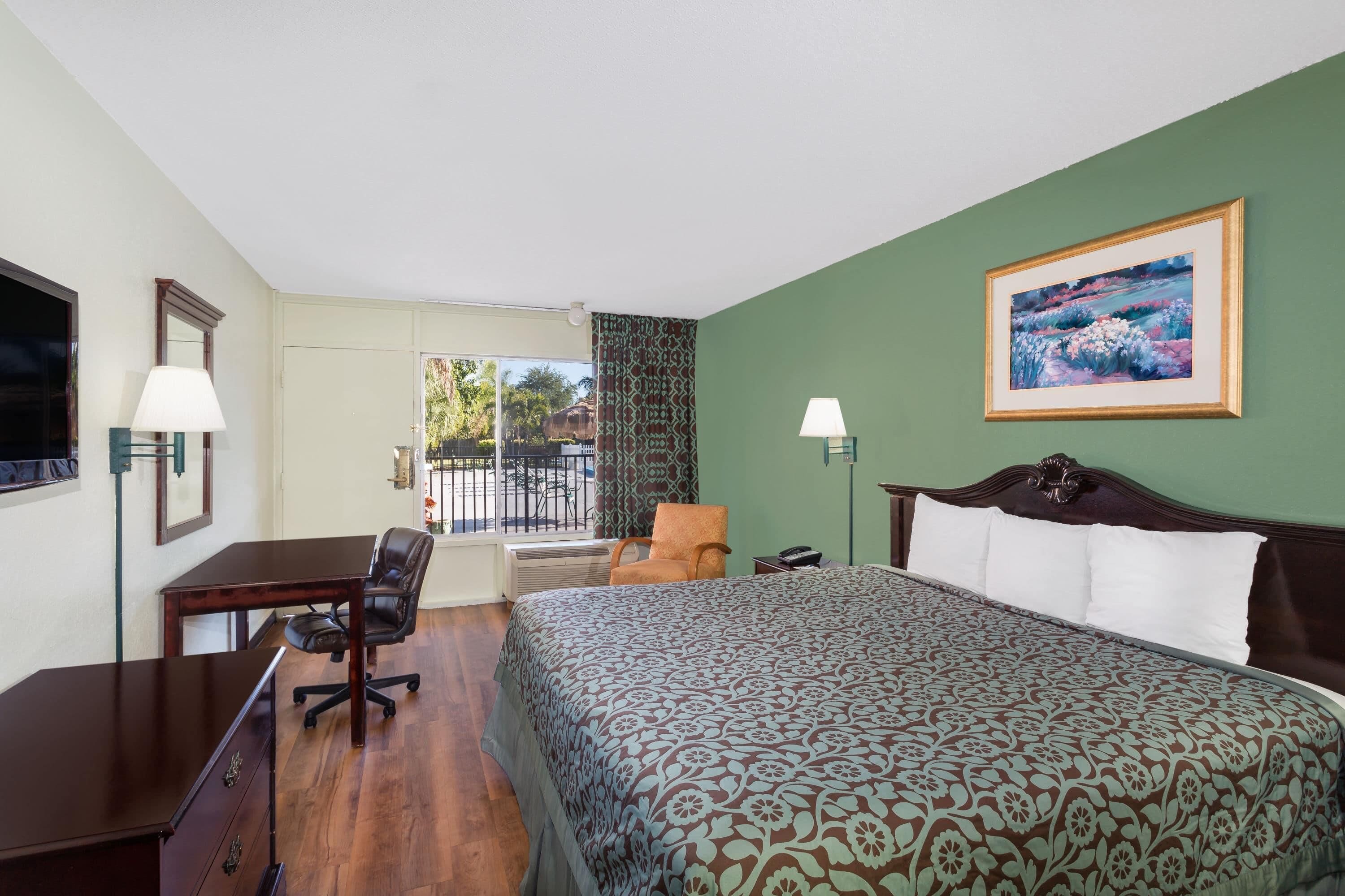 Quarto de hotel com cama, escrivaninha, cadeira e vista para o exterior.