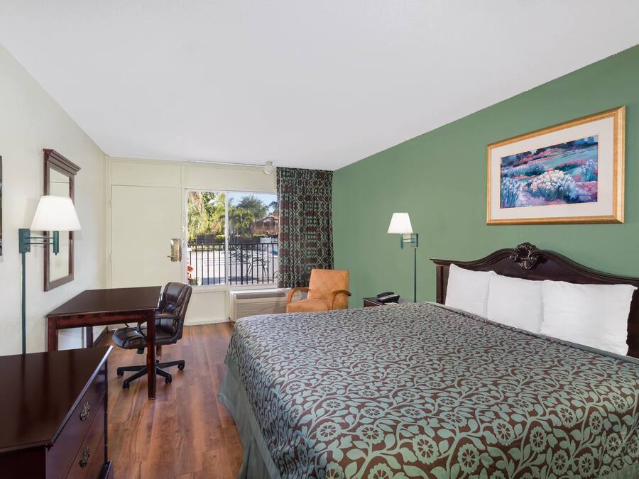 Quarto de hotel com cama, escrivaninha, cadeira e vista para o exterior.