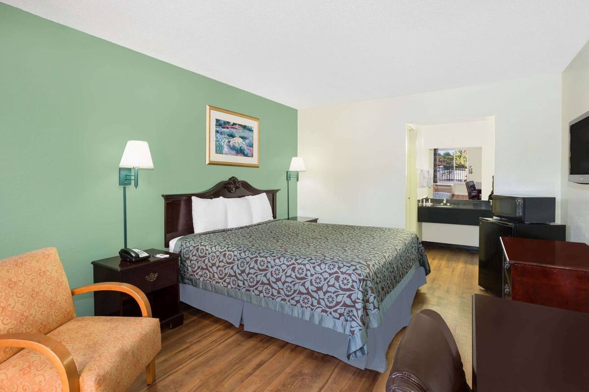 Habitación de hotel con cama, dos mesitas de noche, una silla, escritorio, televisión y kitchenette.
