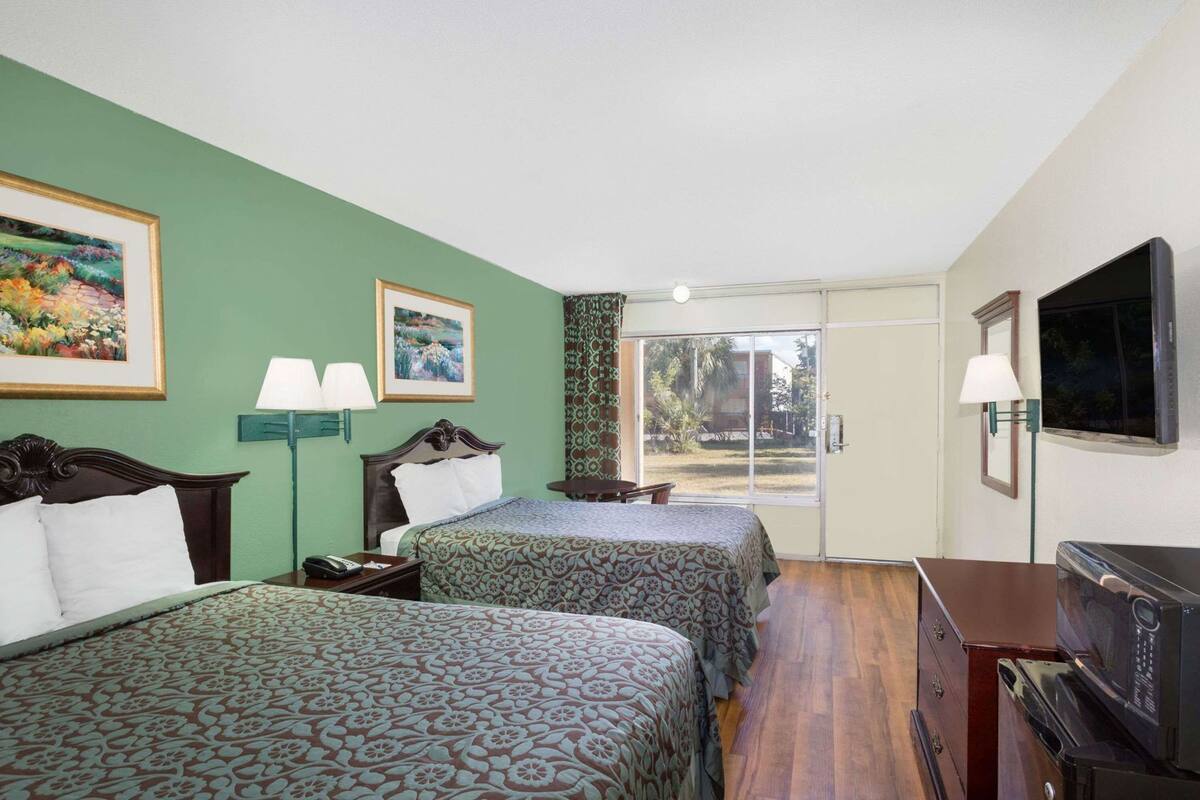 Habitación de hotel con dos camas, televisión, escritorio y vistas al exterior.