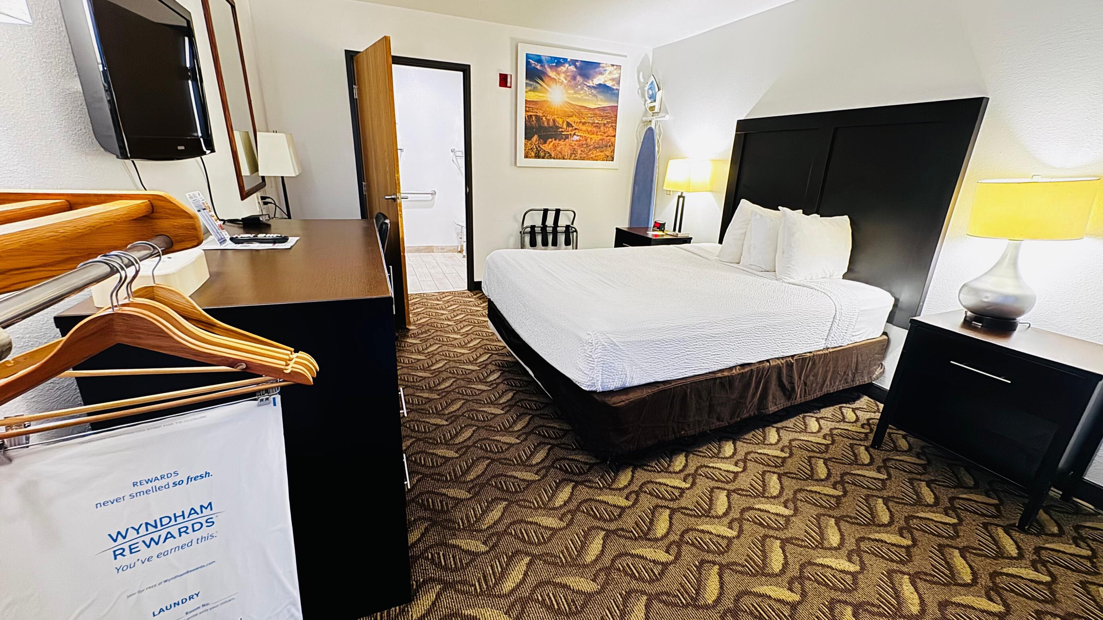 A hotel room with a bed, a desk, a chair, a TV, and a painting on the wall.