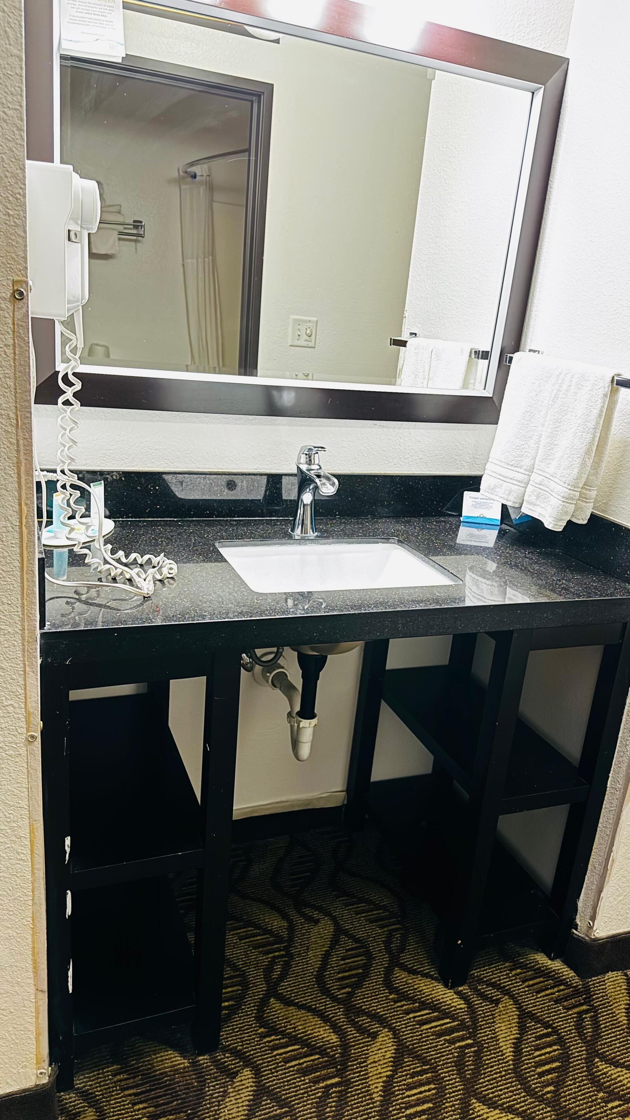 A hotel bathroom with a sink, mirror, towel rack, and a telephone.