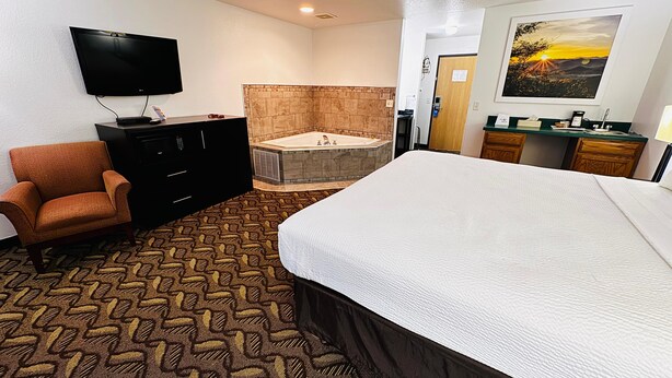 A hotel room with a large bed, a TV, a chair, a desk, a bathroom with a bathtub, and a painting on the wall. - Days Inn by Wyndham North Platte (North Platte)