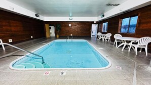 An indoor swimming pool with a diving board, surrounded by white chairs and tables. - Days Inn by Wyndham North Platte (North Platte)