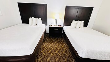 Una habitación de hotel con dos camas, una mesita de noche con lámpara y una alfombra estampada.